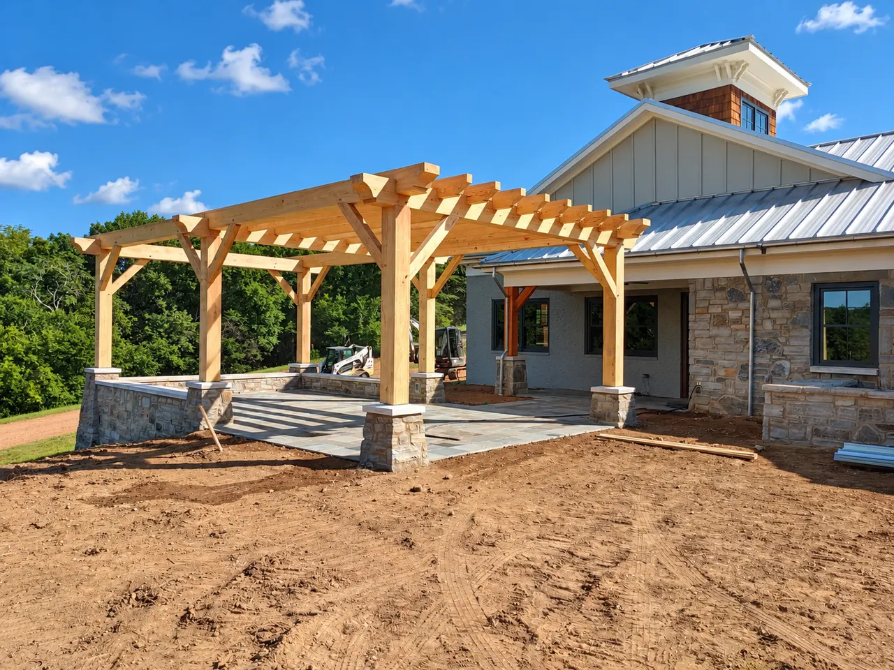 Custom home exterior during grading and hardscape preparation around a timber pergola.