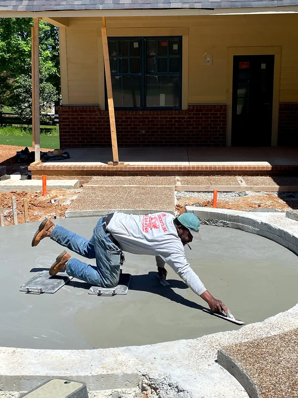 Concrete finishing work in progress on the curved hardscape beside the porch addition.