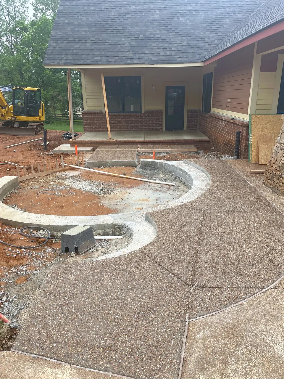 Exposed aggregate concrete and curved hardscape taking shape beside the new porch area.