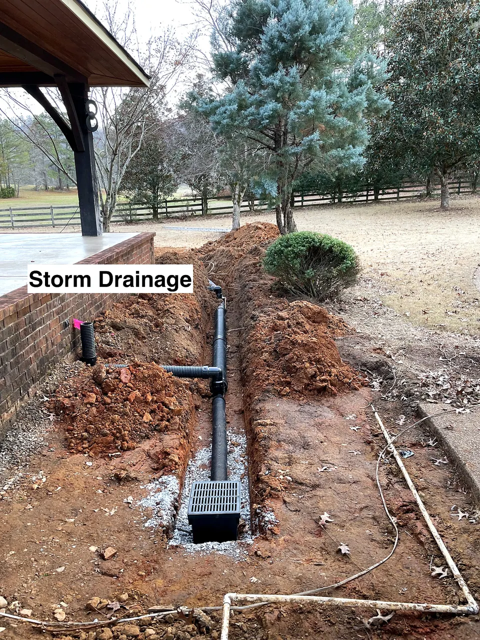 Underground storm drainage installation with catch basin and piping beside a ranch house.