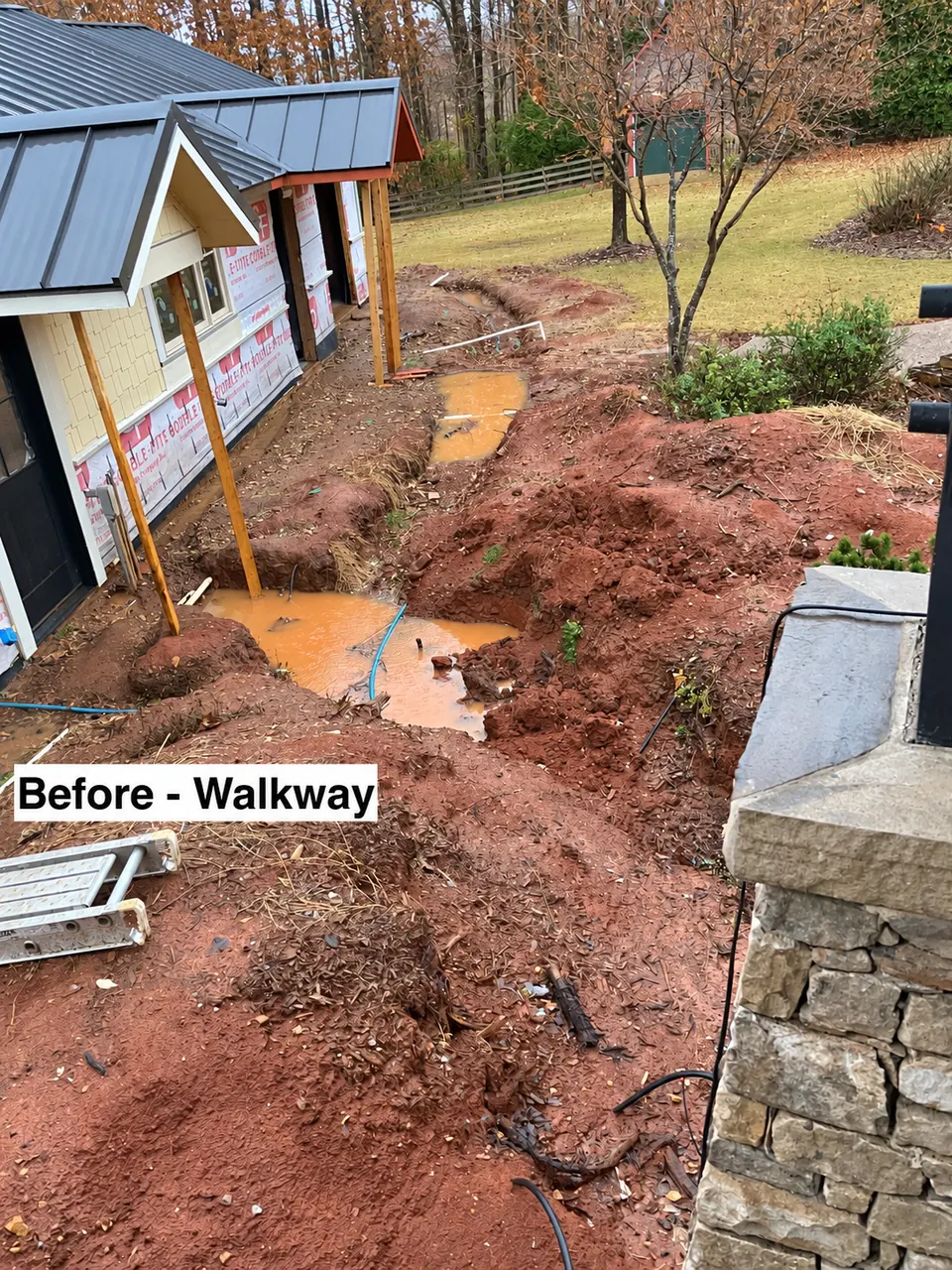 Existing site conditions before excavation and grading for a new stone walkway beside a ranch house.