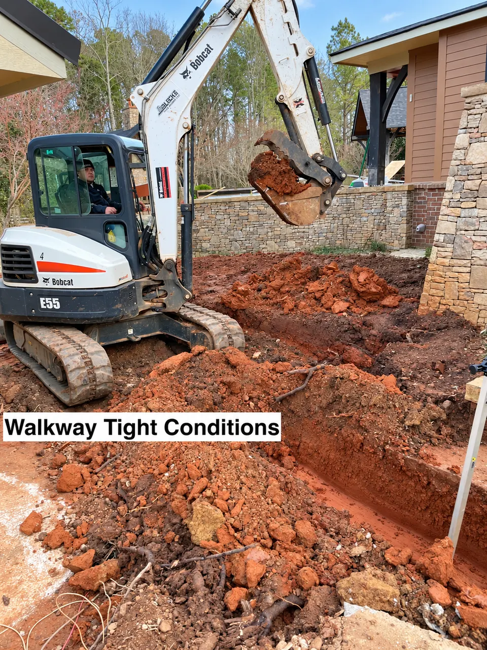 Mini excavator performing tight-access grading beside a ranch house for a new stone walkway.